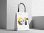 Weisse Tragetasche mit abonax Logo und grafischem Design, die vor einer Betonwand steht.