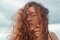 Bildwelt des Hair Stores try: Porträt mit rotblonden Locken im Wind vor wolkigem Himmel